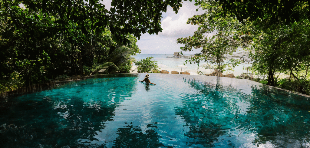 A woman enjoys a refreshing swim in the pristine pool of an all-inclusive resort, basking in the sun's warm glow on a trip planned by My Tailored Escape luxury travel agency.