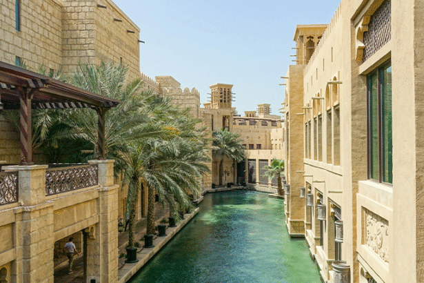 Photo of a sparkling blue creek in the middle of tall sand-colored middle-east inspired buildings.