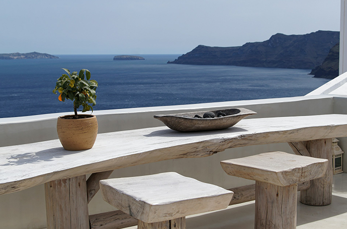 A table and two stools on a balcony with a stunning view of the ocean in the background.