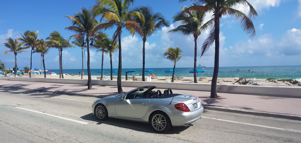 A stylish convertible car cruises along a scenic Miami road, framed by swaying palm trees, capturing the vibrant spirit of the city on a trip planned by My Tailored Escape luxury travel agency.