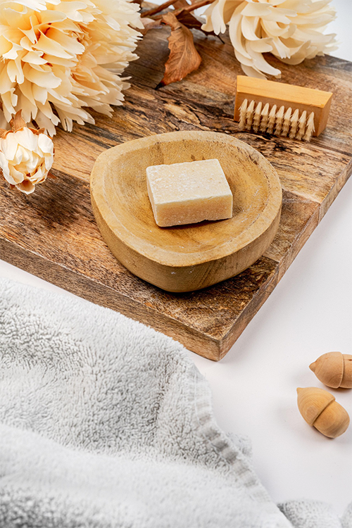 A plush towel with a delicate soap bar rests on it, accompanied by a wooden tray adorned with a single elegant flower.