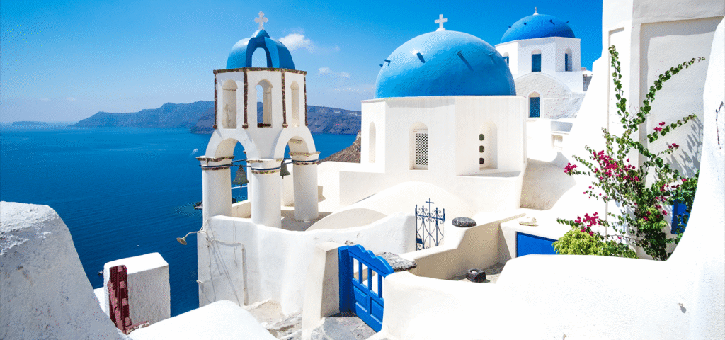 Photo of white buildings with iconic blue dome roofs in Santorini, Greece.