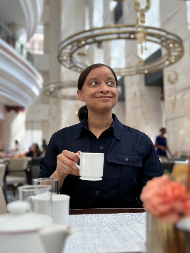 Photo of Antoinette at a table, holding a cup of tea.