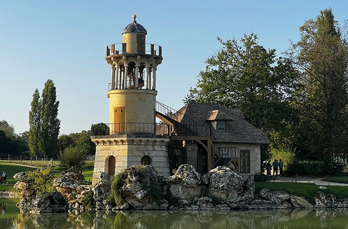 A charming small building topped with a clock tower, set in a serene environment at "The Queen's Hamlet" at the Palace of Versailles.