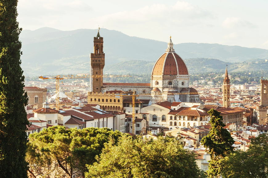 Photo of the Duomo in Florence, Italy peeking behind green trees.