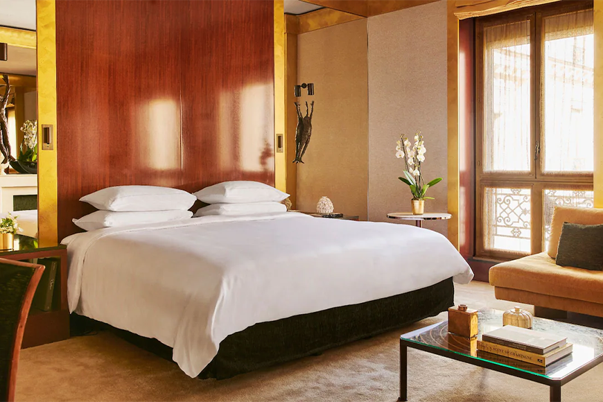 Photo of an elegant modern hotel room and bed with crisp white sheets and a large shiny oak headboard at the Park Hyatt Paris Vendome.