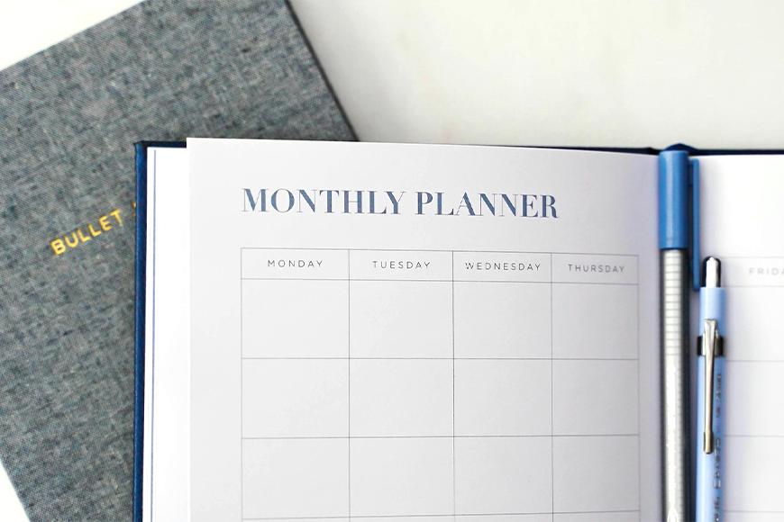 Photo of an open monthly planner notebook in front of a closed bullet journal.