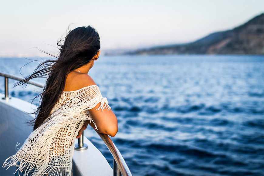 Woman in bohemian dress looking at the beautiful blue water horizon from the edge of a cruise ship.