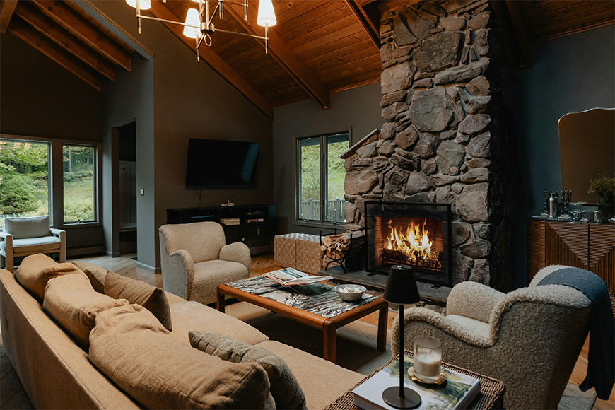 Cozy mountain lodge living room with stone fireplace, vaulted wood ceiling, and plush seating — luxury cabin and mountain retreat vacations planned by My Tailored Escape, boutique travel agency serving Washington DC, Maryland, Virginia and nationwide.