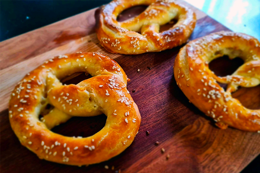 Fresh soft Bavarian pretzels with sesame seeds on a wooden board, a seasonal food to taste in Bavaria, Germany, one of the best fall travel destinations, by My Tailored Escape, boutique travel agency serving Washington DC, Maryland, Virginia and nationwide.