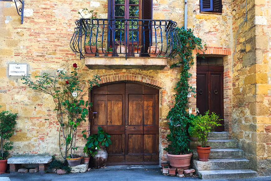 Rustic stone Tuscan villa doorway with terracotta pots, climbing vines, and an iron balcony, a dreamy fall lodging in one of the best fall travel destinations, by My Tailored Escape, boutique travel agency serving Washington DC, Maryland, Virginia and nationwide.