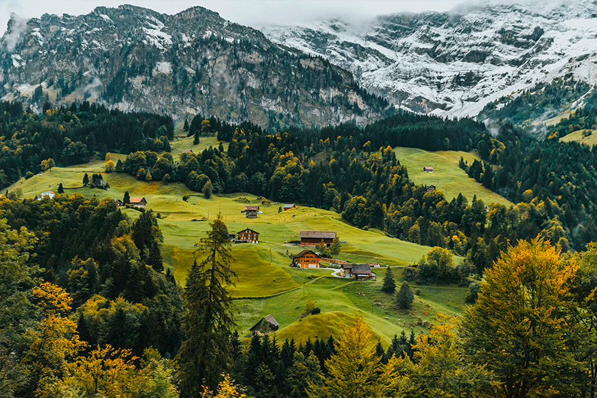 Swiss Alpine valley with golden larch forests, chalets, and snow-dusted peaks near Zermatt, a scenic Glacier Express stop and great place to visit in fall, by My Tailored Escape, boutique travel agency serving Washington DC, Maryland, Virginia and nationwide.